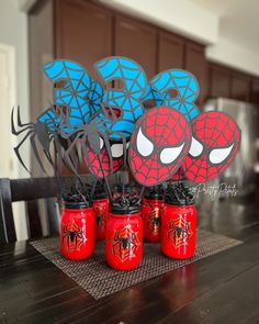 there are some red and blue mason jars with spiderman decorations on top of them