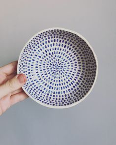 a hand holding a blue and white bowl on top of a gray surface with dots