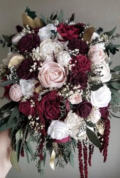 a bridal bouquet with red, white and pink flowers is held by someone's hand