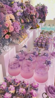 there are many cupcakes on the table with purple frosting and flowers in vases