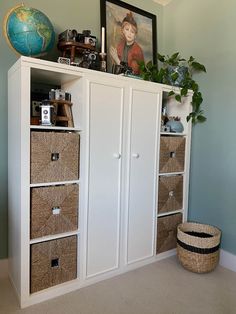 a white cabinet with baskets and pictures on top in a room next to a wall