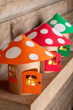 three paper houses sitting on top of a wooden shelf next to a brick wall with candles in them