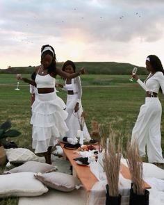 three women in white dresses standing around a table with food and wine glasses on it