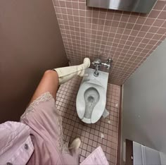 a person cleaning a toilet in a bathroom with pink tiles on the walls and floor