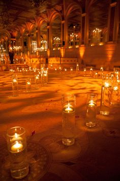 many lit candles are on the floor in a hall