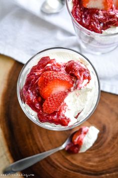 a dessert with strawberries and whipped cream in a glass on a wooden cutting board