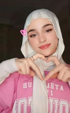 a woman wearing a pink and white hoodie with her hands on her heart shaped finger