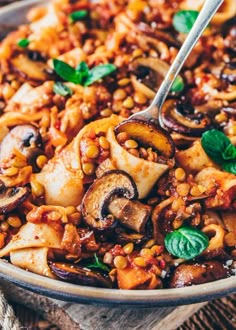 a bowl filled with pasta and mushrooms on top of a wooden table next to a fork