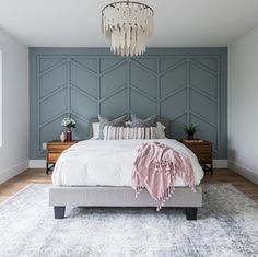 a bedroom with blue walls and white bedding, chandelier hanging from the ceiling