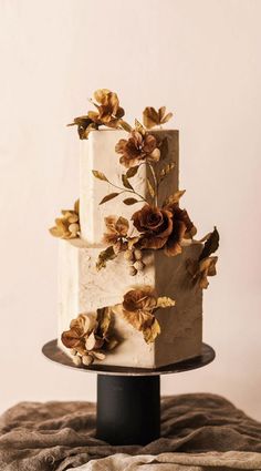 a three tiered white cake with flowers on the top and bottom, sitting on a black stand