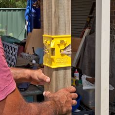 a man holding onto a wooden post with a yellow box on it's side