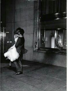 black and white photograph of a man carrying a woman on his back in front of a building