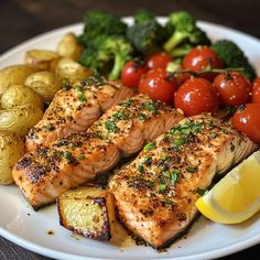 a white plate topped with salmon, potatoes and broccoli next to lemon wedges