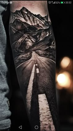 a man with a black and white tattoo on his arm that has mountains in the background