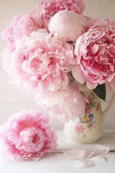 pink peonies are in a white vase on a table next to some petals