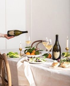 a woman pouring wine into a glass at a table with food and drinks on it