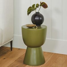 a black vase sitting on top of a green table next to a plant in a pot