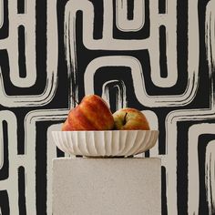 two apples sitting in a white bowl on top of a pedestal against a black and white wall