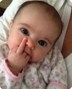 a baby laying on top of a bed holding it's hand up to its mouth