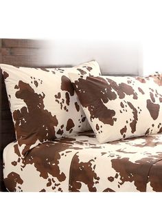 a brown and white cow print bed spread on a wooden headboard with two pillows