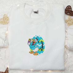 Introducing our adorable Donald Duck With Easter Chick Embroidered Shirt! This charming Disney-inspired shirt showcases a delightful embroidery of Donald Duck holding a cute Easter chick. Made with high-quality materials, it offers superior comfort and durability. With its vibrant colors and meticulous detailing, this shirt is perfect for Disney enthusiasts of all ages. Whether you’re [...] Chick Shirt, Perfect Thanksgiving, Easter Chick, Bustling City, Best Mothers Day Gifts, Cartoon Gift, St Patrick's Day Gifts, Easter Chicks, Sports Hoodies