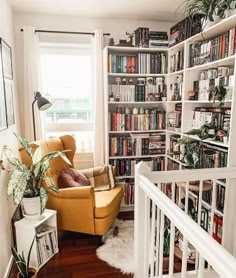 a living room filled with lots of books on top of a book shelf next to a stair case