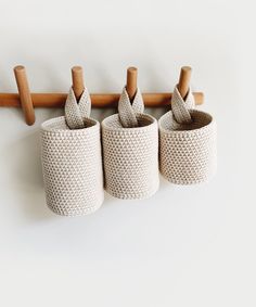 three white baskets are hanging on a coat rack with two wooden pegs attached to them