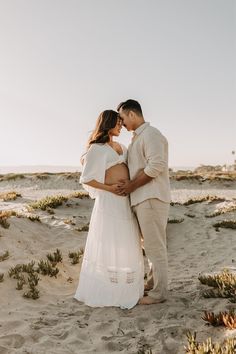 a man and woman standing in the sand with their arms around each other, kissing