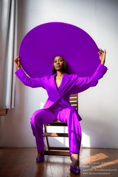 a woman in a purple suit sitting on a chair holding a large round object over her head