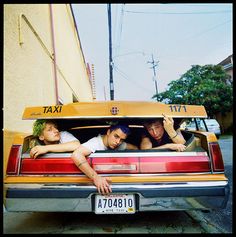 three young men sitting in the back of a yellow taxi with their arms around each other