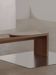 a wooden table sitting on top of a white floor next to a vase and potted plant