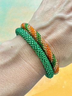 a woman's hand with two bracelets on her left wrist and an orange, green, and white beaded bracelet on her right arm