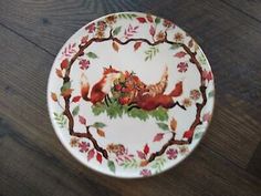 a white plate with red foxes on it sitting on top of a wooden table next to a