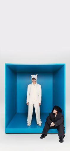 two people in white suits and black hats are sitting in a blue box with one person dressed as a cat