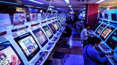 several people playing video games in a room full of arcade machines and gaming screens on the walls