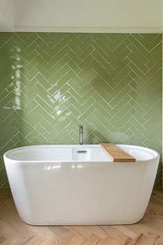 a white bath tub sitting on top of a wooden floor next to a green tiled wall