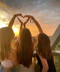 three girls making a heart with their hands while the sun is setting in the background