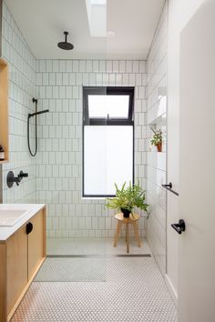 a white tiled bathroom with a plant in the window and sink area next to it