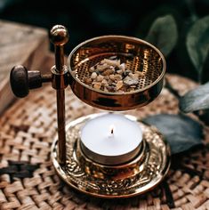 a candle that is sitting on top of a stand with rocks in the bowl and some leaves around it