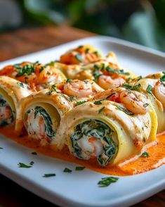 a white plate topped with rolls covered in sauce and shrimp on top of spinach