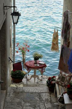 an alley way leading to the water with flowers and clothes hanging on hooks above it