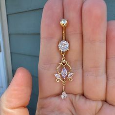 a person is holding a gold belly ring with two diamonds on the end and a flower design dangling from it