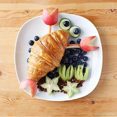 a croissant on a plate with fruit and vegetables in the shape of eyes