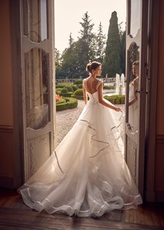 a woman in a wedding dress is standing at an open door with her back to the camera