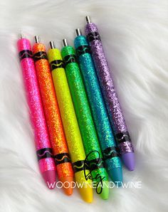 four different colored glitter pens are lined up in a row on a white fur surface