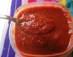 a spoon full of sauce sitting on top of a plastic container filled with red sauce