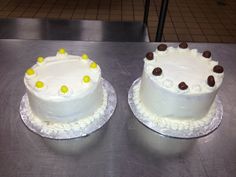 two white cakes sitting on top of a metal table next to each other with yellow and brown decorations