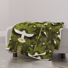 a green blanket with white birds and leaves on it in the middle of a living room