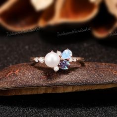 a close up of a ring with pearls and stones on a piece of wood next to some shells