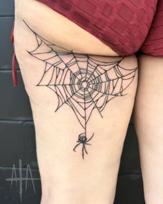 a spider web tattoo on the back of a woman's thigh, with her legs crossed